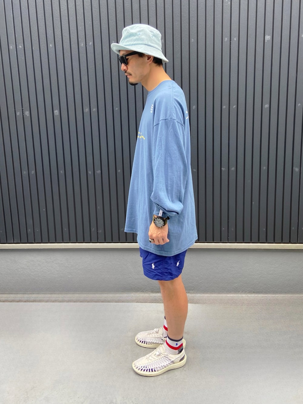 ブルー系のTシャツ/カットソー、ホワイト系のサンダル、ブルー系のハットを着用したメンズの夏コーディネートの2枚目の写真