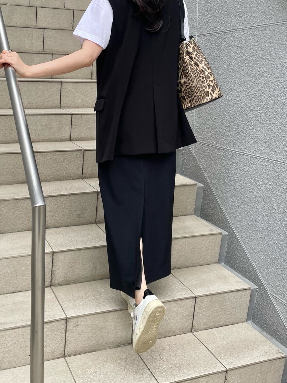 ブラック系のスカート、ブラック系のベスト、ブラウン系のトートバッグを着用したレディースの春コーディネートの5枚目の写真