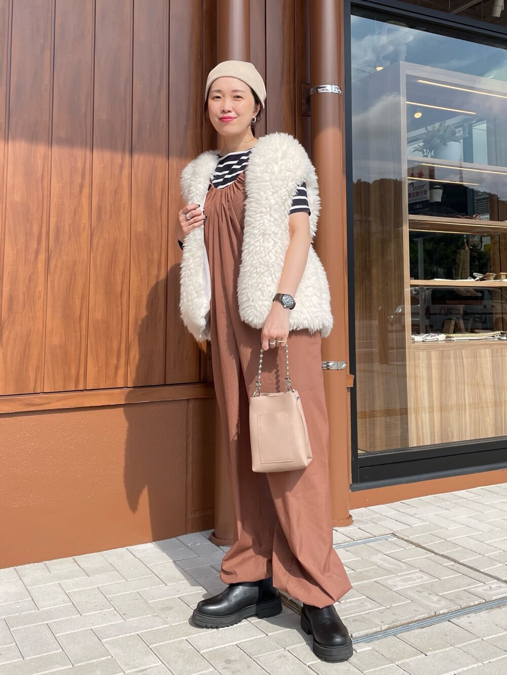 ホワイト系のベスト、ベージュ系のショルダーバッグ、ブラック系のブーツを着用したレディースの秋コーディネートの2枚目の写真