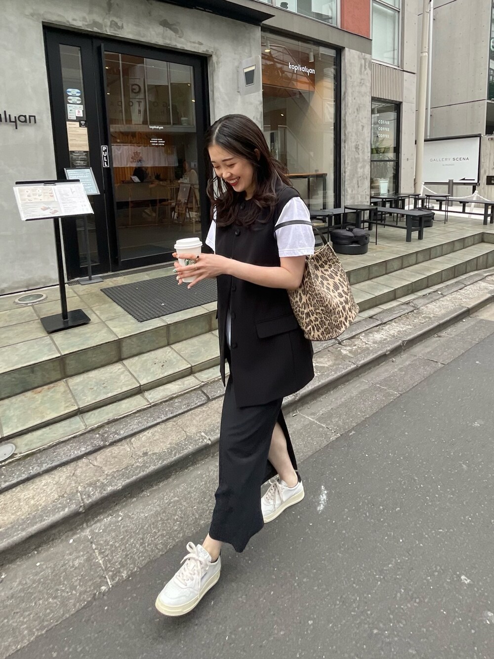 ブラック系のスカート、ブラック系のベスト、ブラウン系のトートバッグを着用したレディースの春コーディネートの2枚目の写真