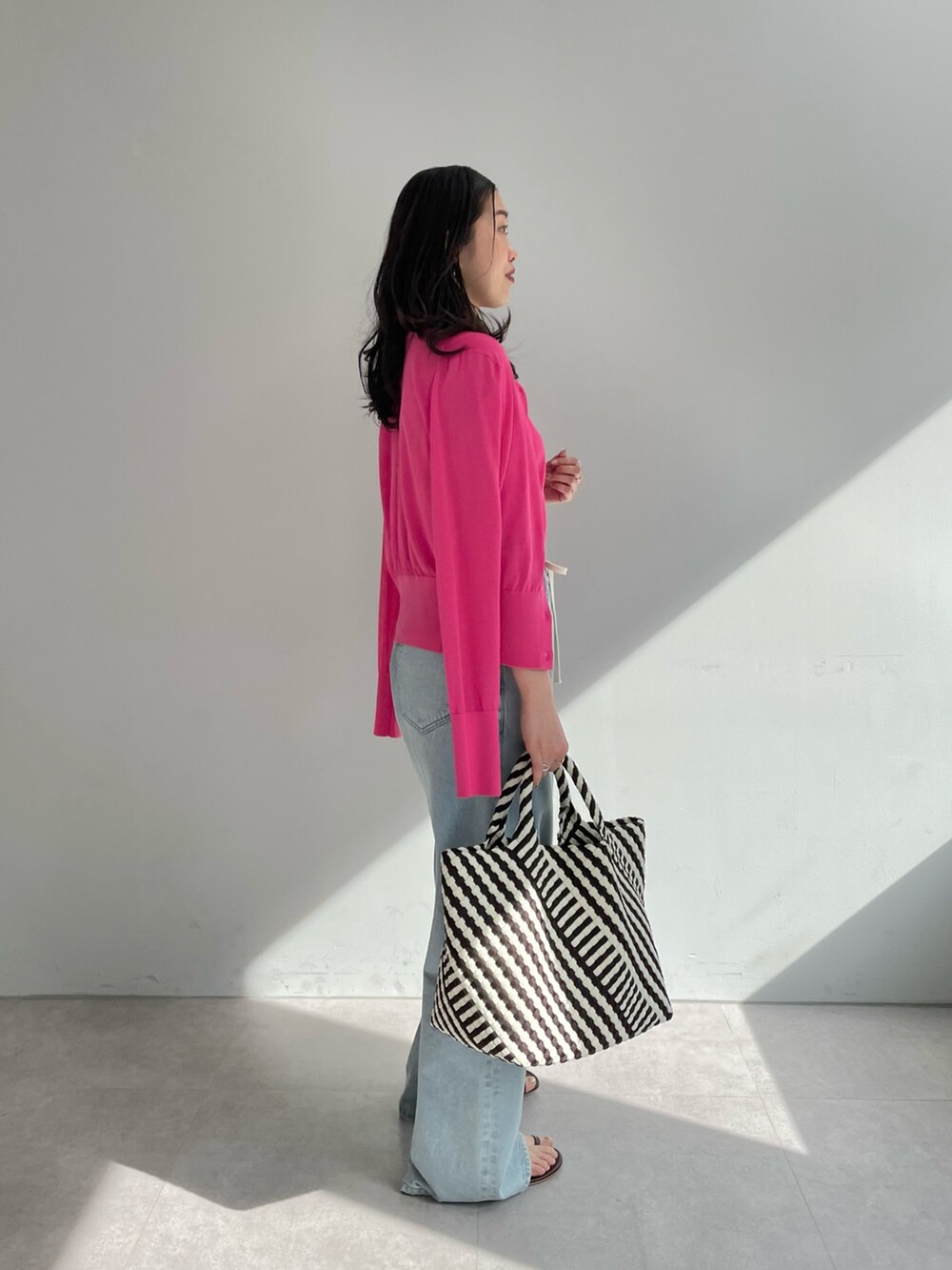 ブルー系のデニムパンツ、ブラック系のトートバッグ、ピンク系のニット/セーターを着用したレディースの春コーディネートの2枚目の写真