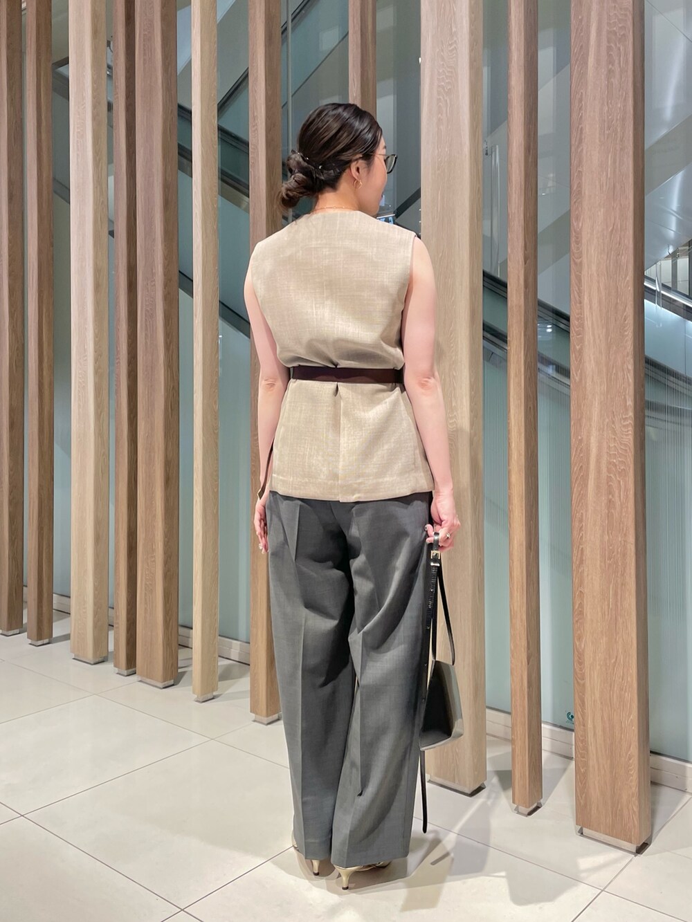 ベージュ系のベスト、ブラック系のショルダーバッグ、グレー系のスラックスを着用したレディースの春コーディネートの2枚目の写真