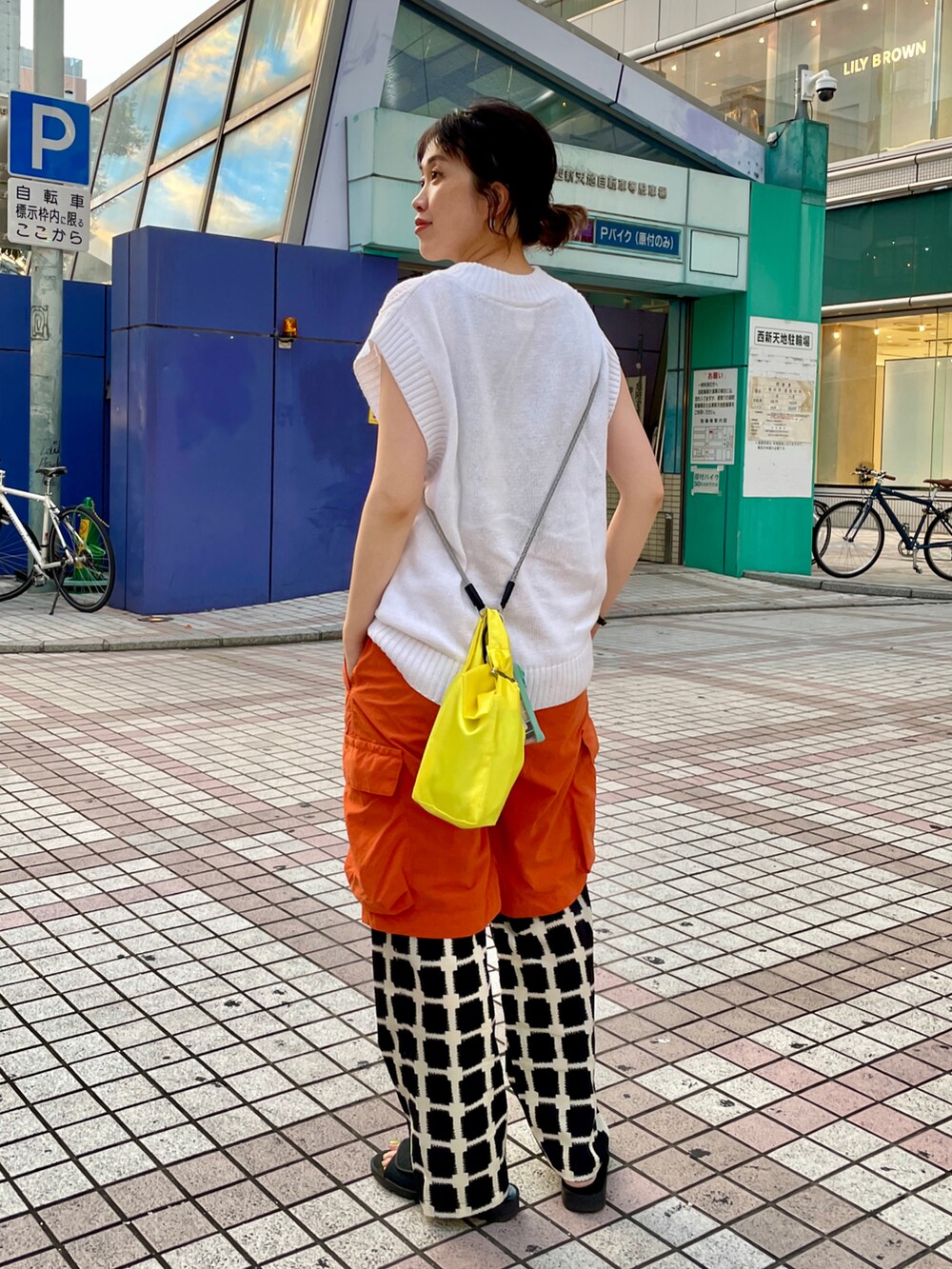 ブラック系のサンダル、ホワイト系のスラックス、オレンジ系のパンツを着用したレディースの夏コーディネートの2枚目の写真