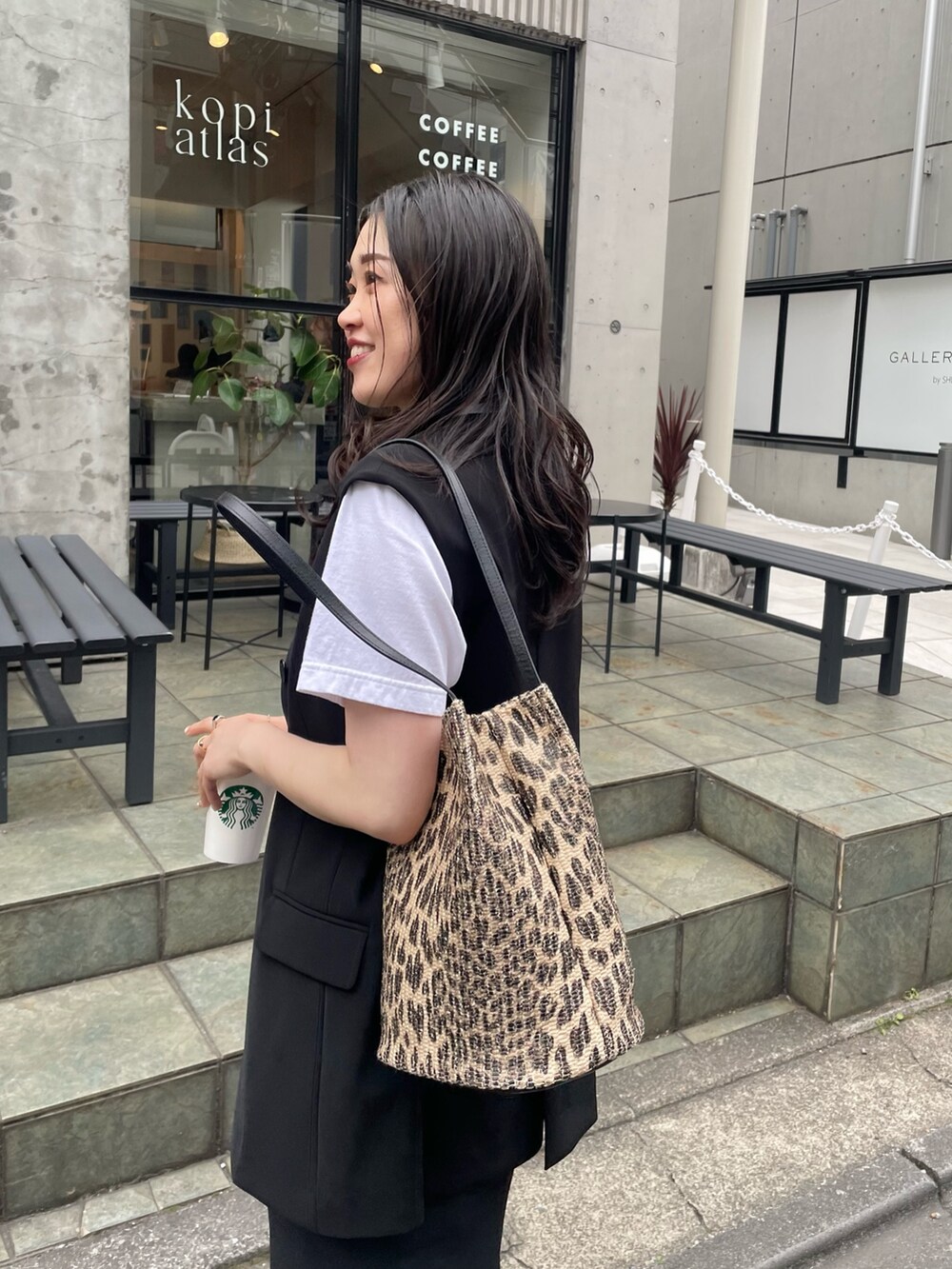 ブラック系のスカート、ブラック系のベスト、ブラウン系のトートバッグを着用したレディースの春コーディネートの4枚目の写真