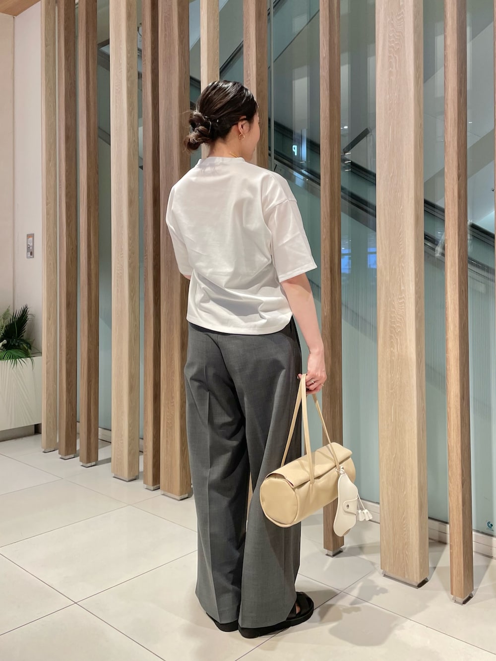 グレー系のスラックス、ベージュ系のハンドバッグ、ブラック系のサンダルを着用したレディースの春コーディネートの2枚目の写真