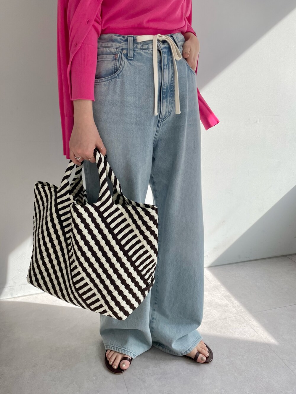 ブルー系のデニムパンツ、ブラック系のトートバッグ、ピンク系のニット/セーターを着用したレディースの春コーディネートの5枚目の写真