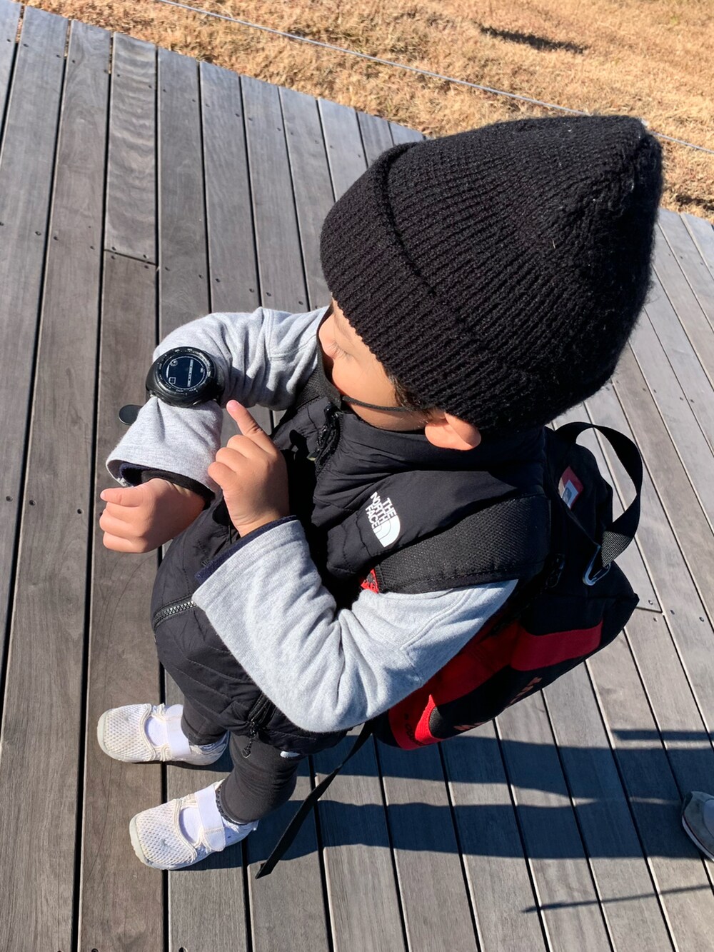 ブラック系のバックパック/リュック、ブラック系のダウンベスト、ホワイト系のスニーカーを着用したキッズの秋コーディネートの4枚目の写真