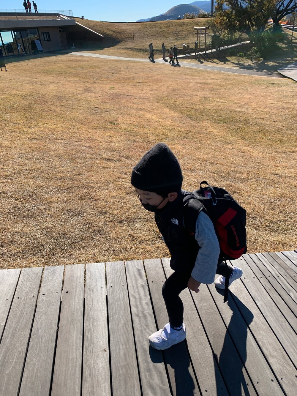 ブラック系のバックパック/リュック、ブラック系のダウンベスト、ホワイト系のスニーカーを着用したキッズの秋コーディネートの2枚目の写真