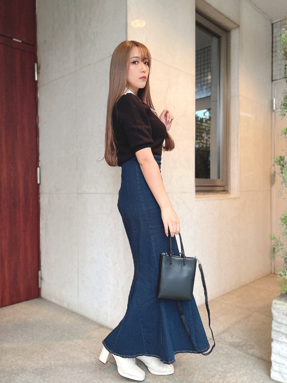 ブラック系のニット/セーター、ブルー系のデニムスカート、ブラック系のショルダーバッグを着用したレディースの春コーディネートの2枚目の写真