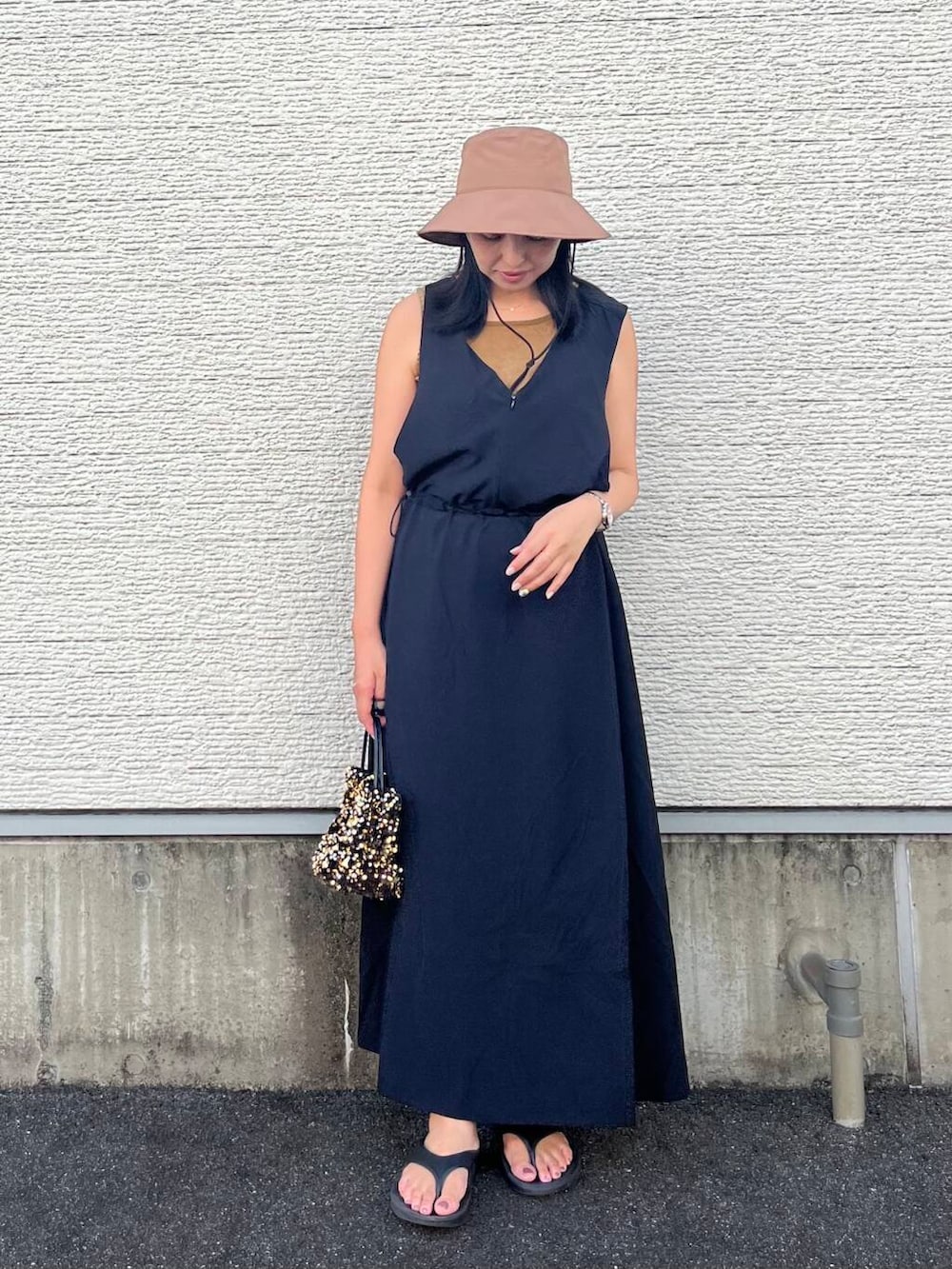 ゴールド系のショルダーバッグ、ブラック系のワンピース、ベージュ系のタンクトップを着用したレディースの夏コーディネートの4枚目の写真