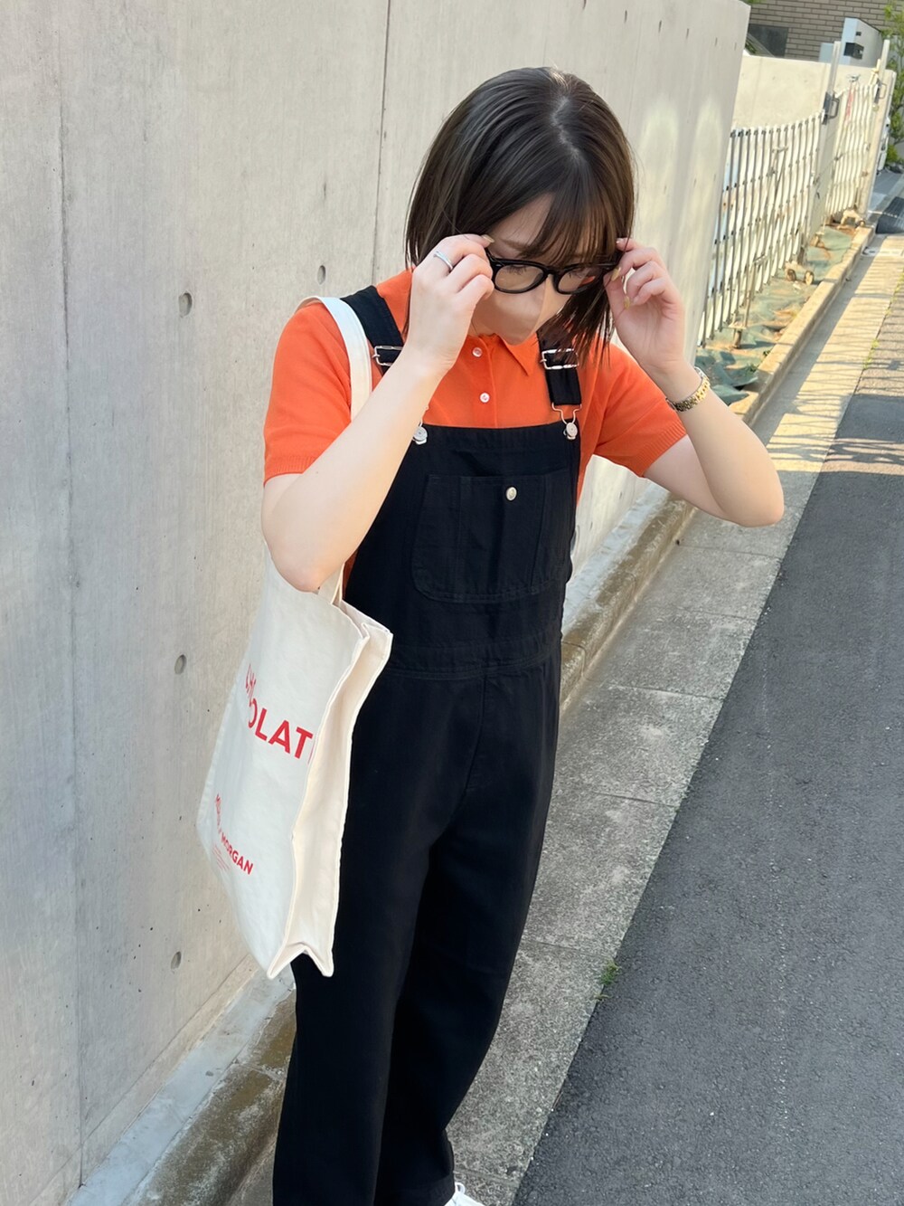 オレンジ系のポロシャツ、ブラック系のサロペット/オーバーオール、ホワイト系のスニーカーを着用したレディースの春コーディネートの3枚目の写真