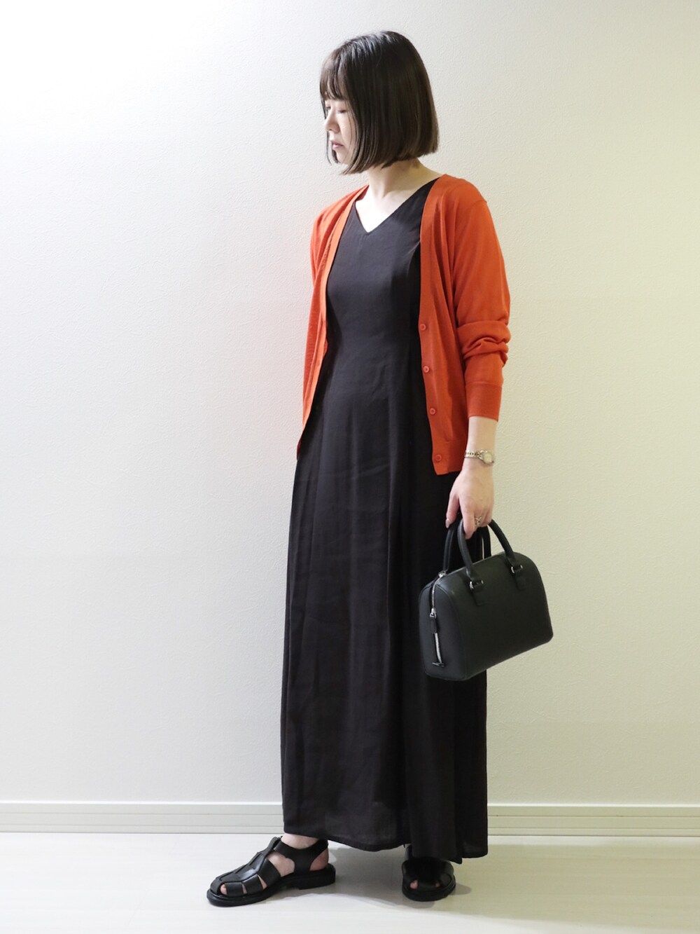オレンジ系のカーディガン/ボレロ、ブラック系のワンピース、ブラック系のボストンバッグを着用したレディースの夏コーディネートの2枚目の写真