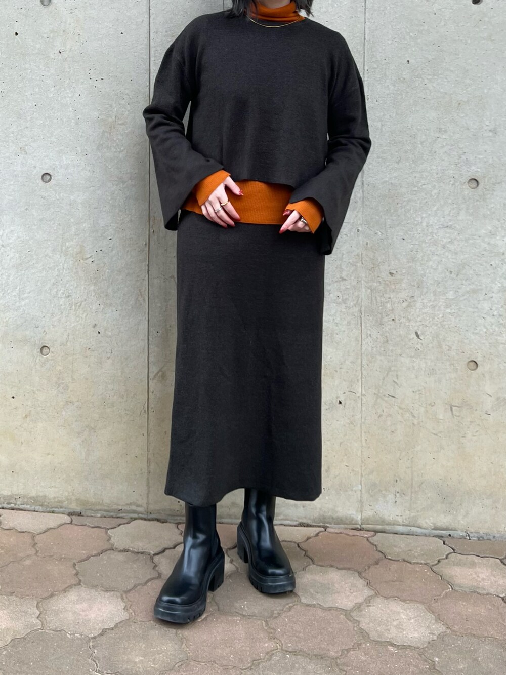 ブラック系のスカート、ブラック系のニット/セーター、オレンジ系のニット/セーターを着用したレディースの冬コーディネートの2枚目の写真