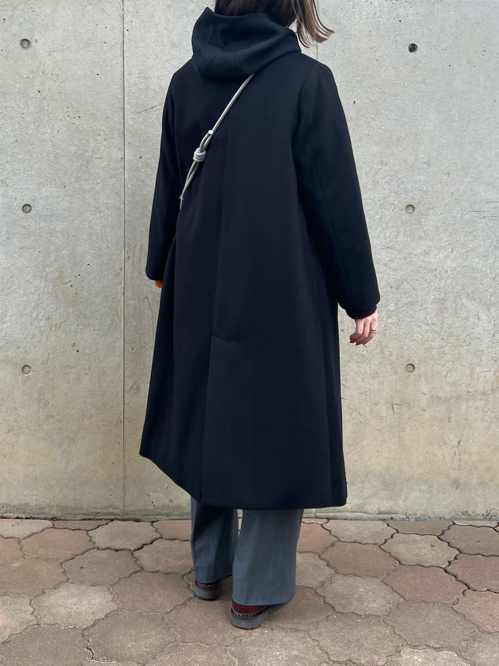 ブラック系のノーカラーコート、オレンジ系のニット/セーター、グレー系のショルダーバッグを着用したレディースの冬コーディネートの3枚目の写真