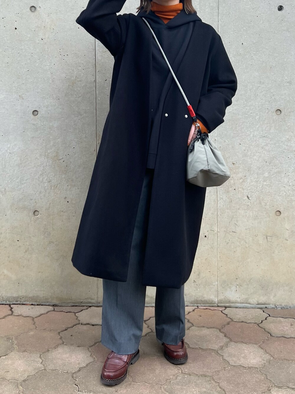 ブラック系のノーカラーコート、オレンジ系のニット/セーター、グレー系のショルダーバッグを着用したレディースの冬コーディネートの2枚目の写真