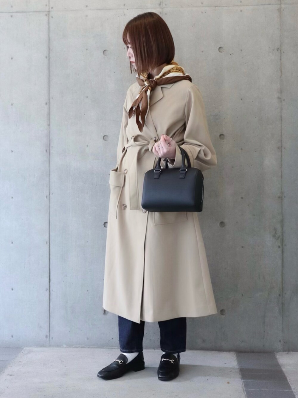 ベージュ系のトレンチコート、ブルー系のデニムパンツ、ブラック系のローファーを着用したレディースの冬コーディネートの2枚目の写真