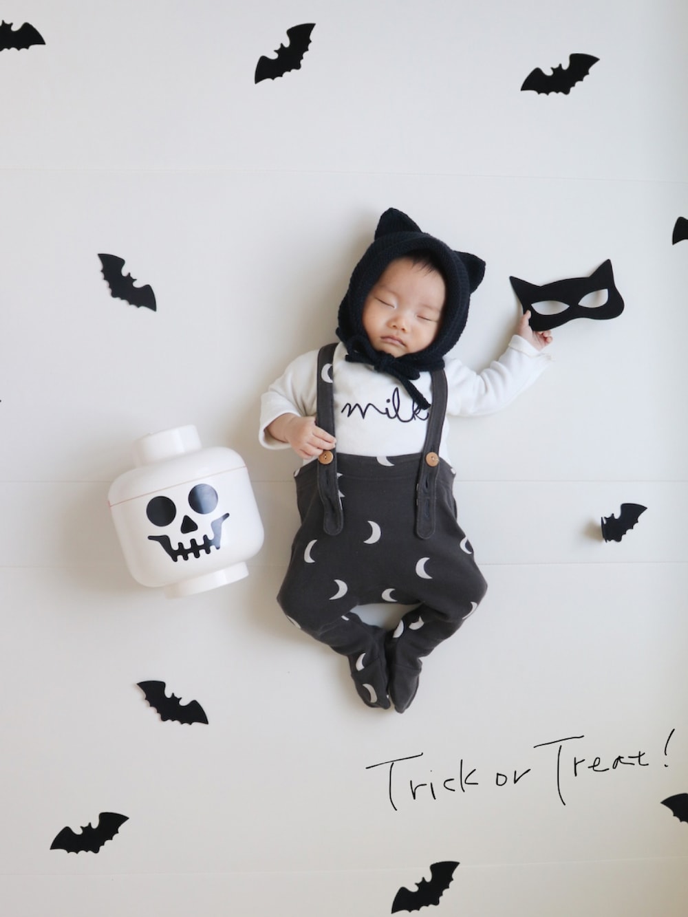 ブラック系の帽子、ベージュ系のロンパース、ブラック系のロンパースを着用したキッズの秋コーディネートの2枚目の写真