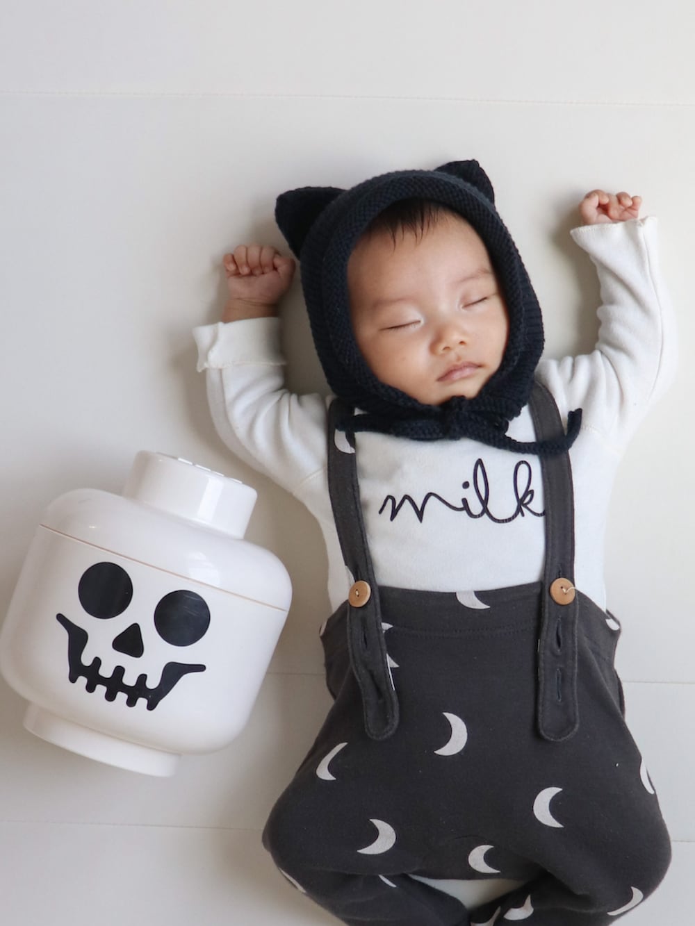 ブラック系の帽子、ベージュ系のロンパース、ブラック系のロンパースを着用したキッズの秋コーディネートの3枚目の写真