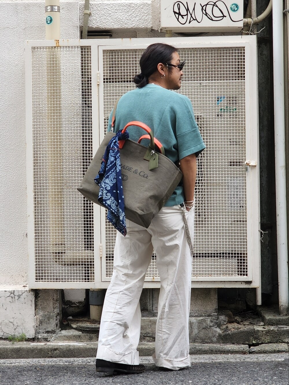 グリーン系のニット/セーター、グリーン系のバッグ、ホワイト系のパンツを着用したメンズの春コーディネートの3枚目の写真