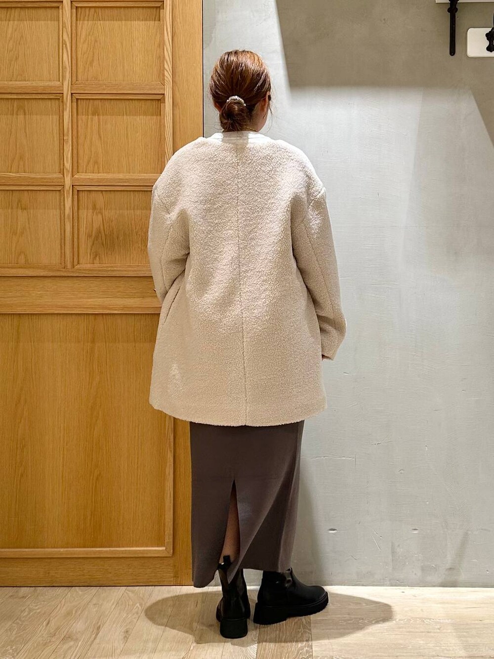 グレー系のスカート、ベージュ系のノーカラーコート、ブラック系のブーツを着用したレディースの秋コーディネートの3枚目の写真