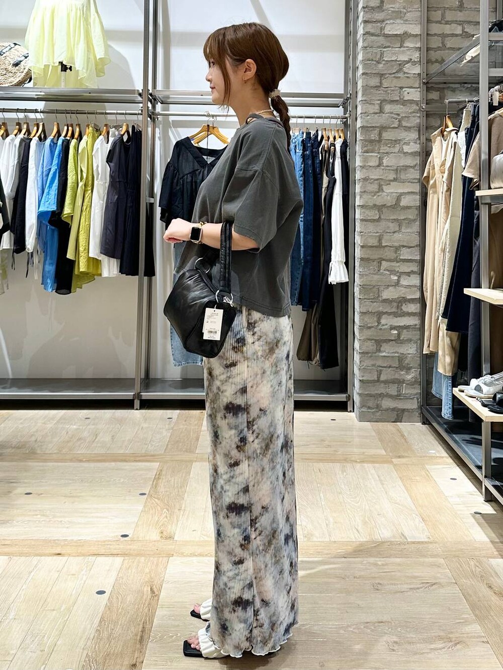 ブラック系のハンドバッグ、ホワイト系のサンダル、グレー系のTシャツ/カットソーを着用したレディースの夏コーディネートの2枚目の写真