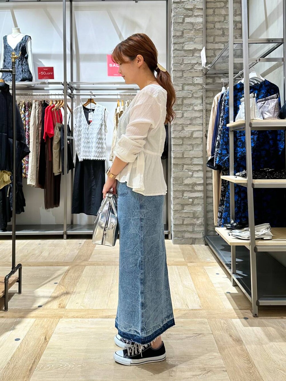 シルバー系のボストンバッグ、ブルー系のデニムスカート、ホワイト系のシャツ/ブラウスを着用したレディースの夏コーディネートの2枚目の写真