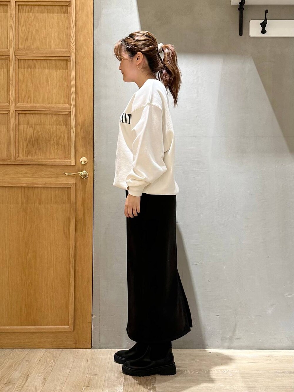 ブラック系のスカート、ブラック系のブーツ、ホワイト系のスウェットを着用したレディースの秋コーディネートの2枚目の写真