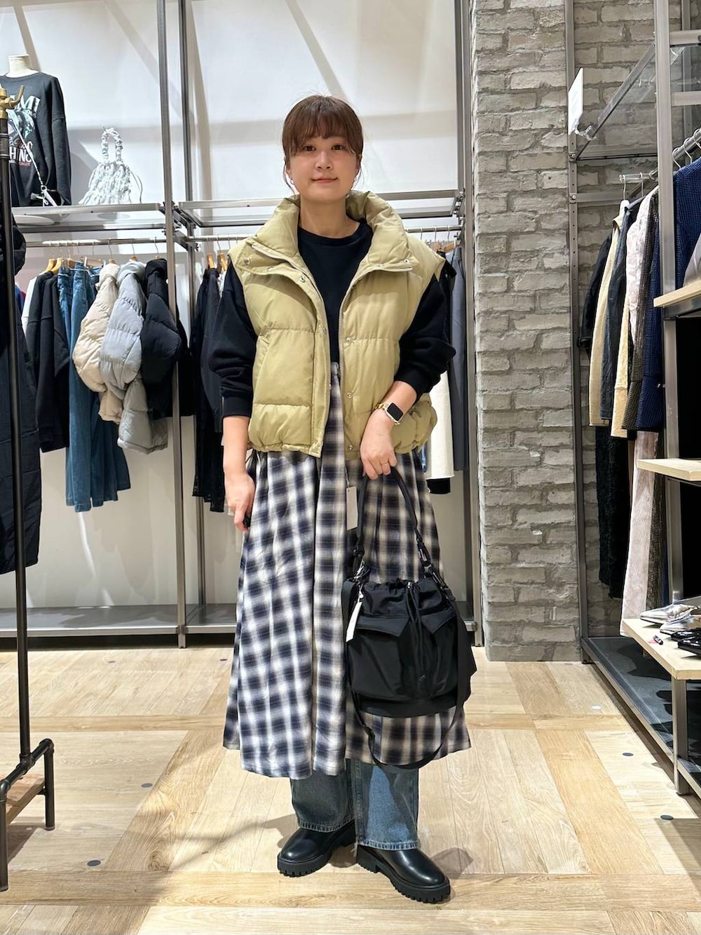 ブラック系のショルダーバッグ、ブルー系のデニムパンツ、ベージュ系のダウンベストを着用したレディースの秋コーディネートの2枚目の写真