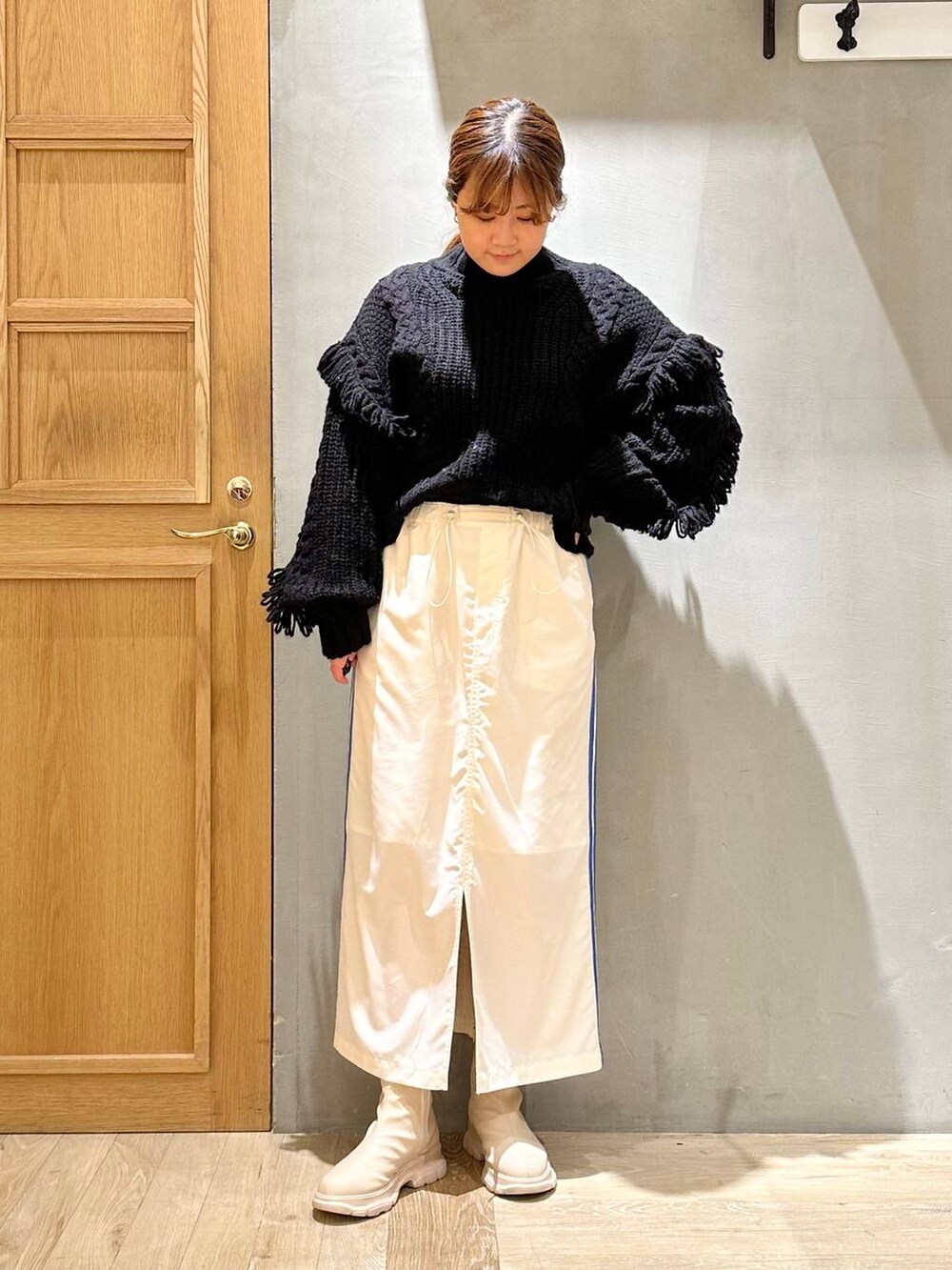 ブラック系のニット/セーター、ホワイト系のブーツ、ホワイト系のスカートを着用したレディースの冬コーディネートの2枚目の写真