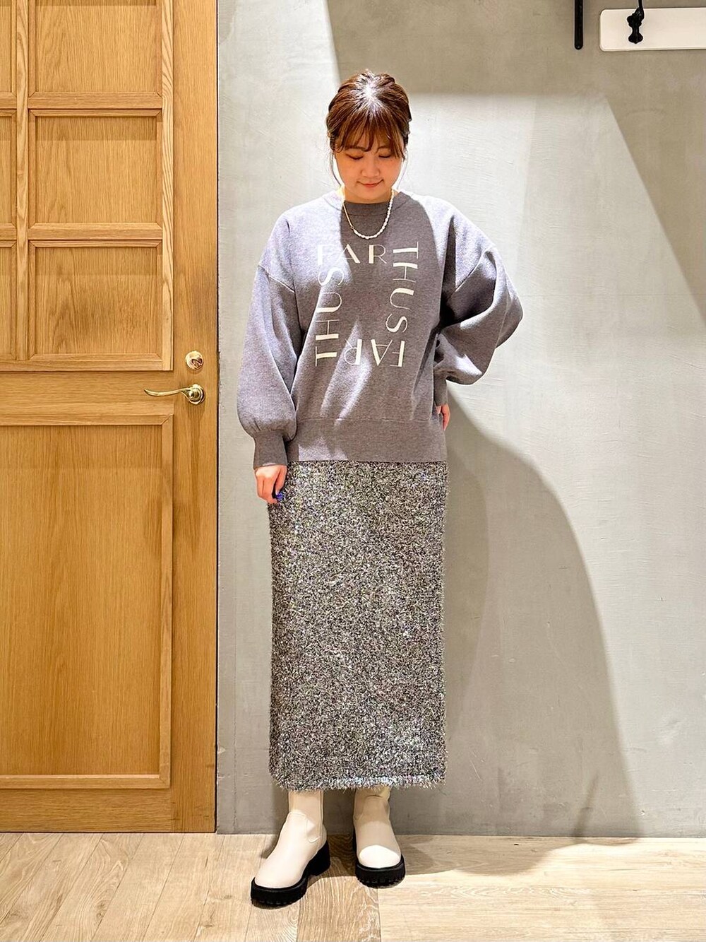 ホワイト系のブーツ、グレー系のニット/セーター、ブラック系のスカートを着用したレディースの冬コーディネートの2枚目の写真