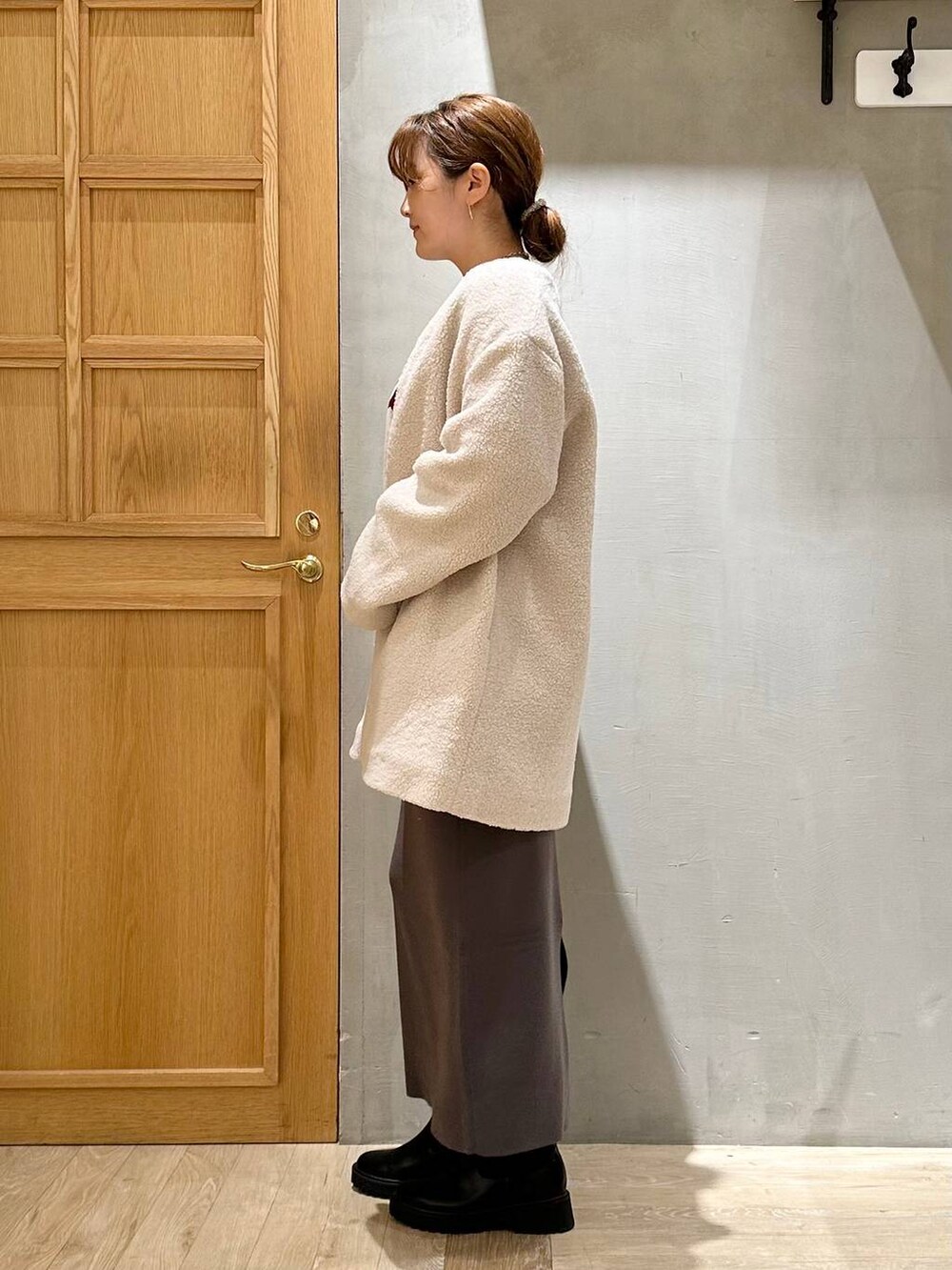 グレー系のスカート、ベージュ系のノーカラーコート、ブラック系のブーツを着用したレディースの秋コーディネートの2枚目の写真