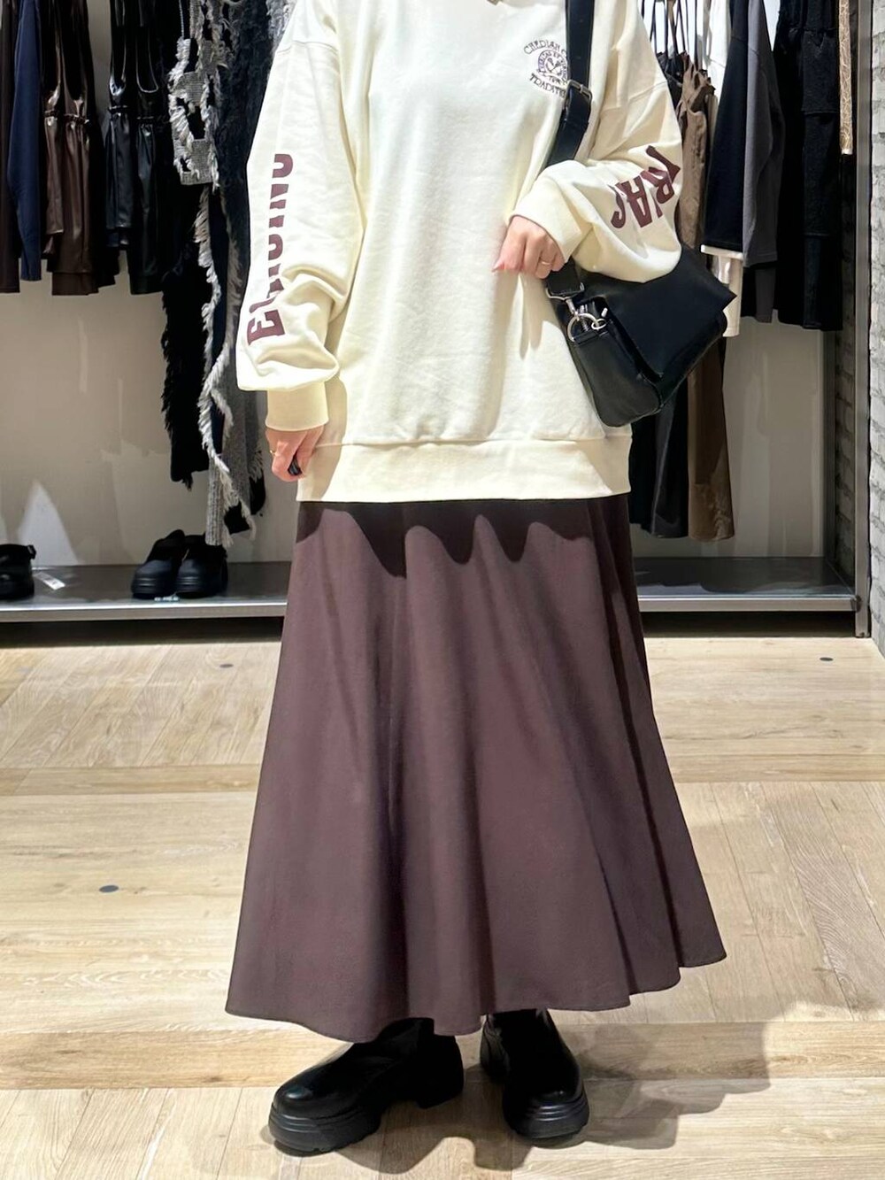 ブラック系のショルダーバッグ、ブラウン系のスカート、ブラック系のブーツを着用したレディースの秋コーディネートの5枚目の写真