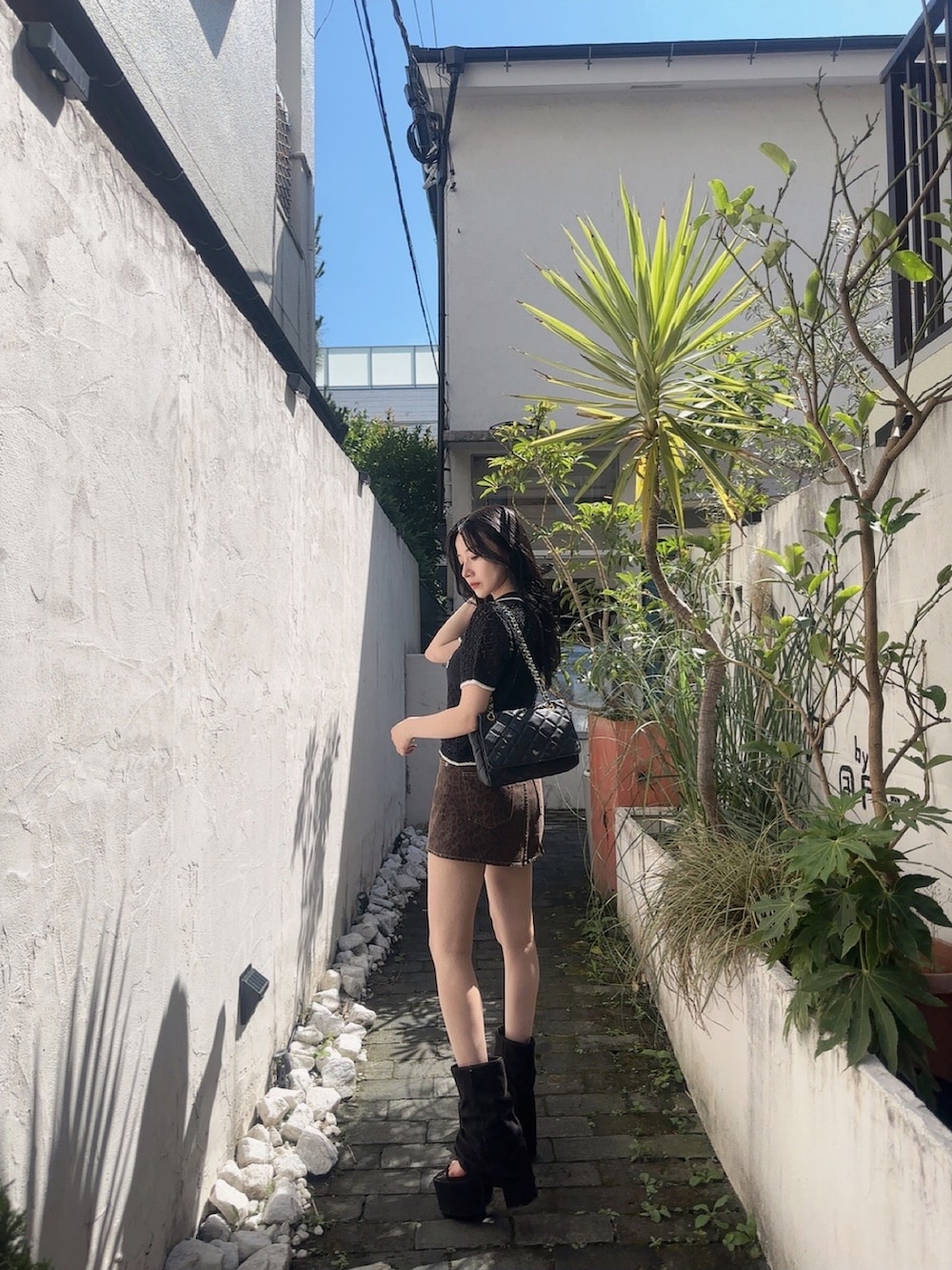 ブラック系のポロシャツ、ブラウン系のスカート、ブラック系のサンダルを着用したレディースの秋コーディネートの4枚目の写真