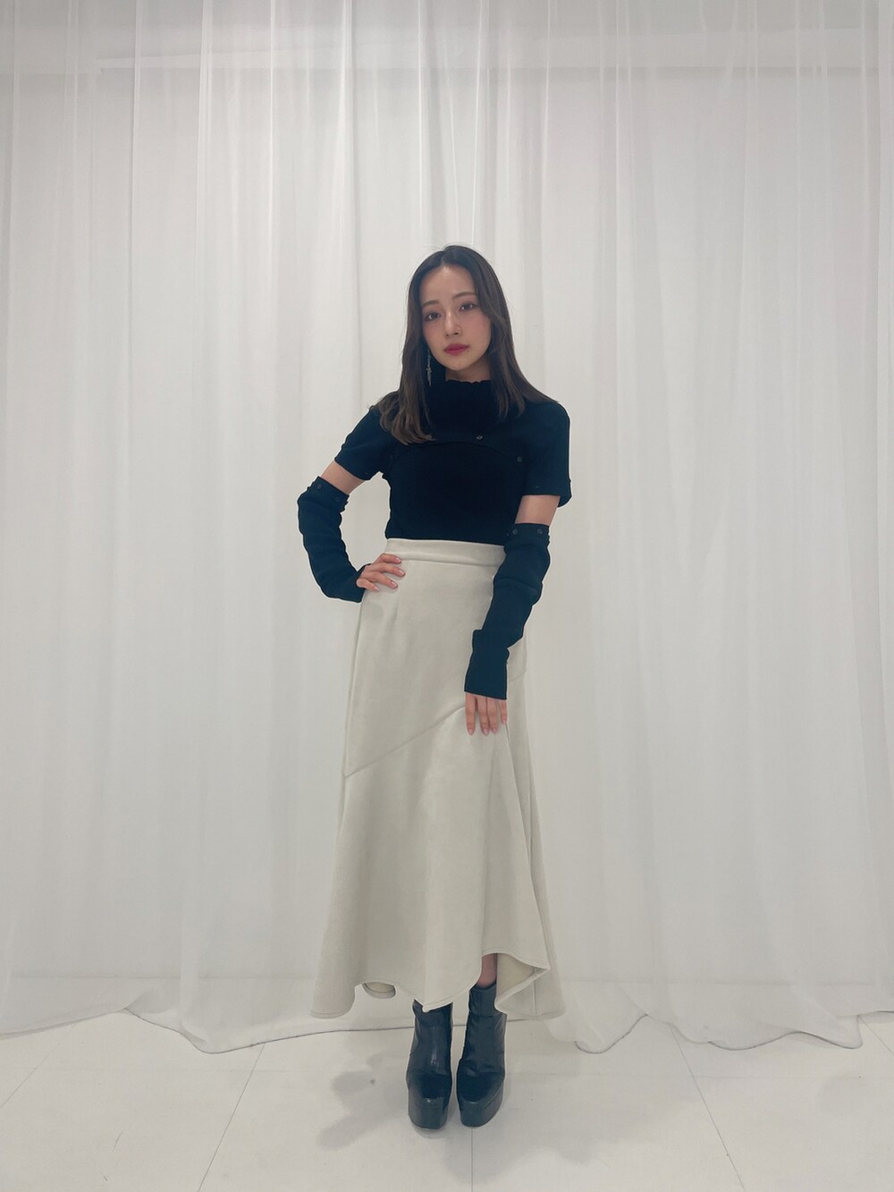 ブラック系のニット/セーター、ホワイト系のスカート、ブラック系のブーツを着用したレディースの春コーディネートの2枚目の写真