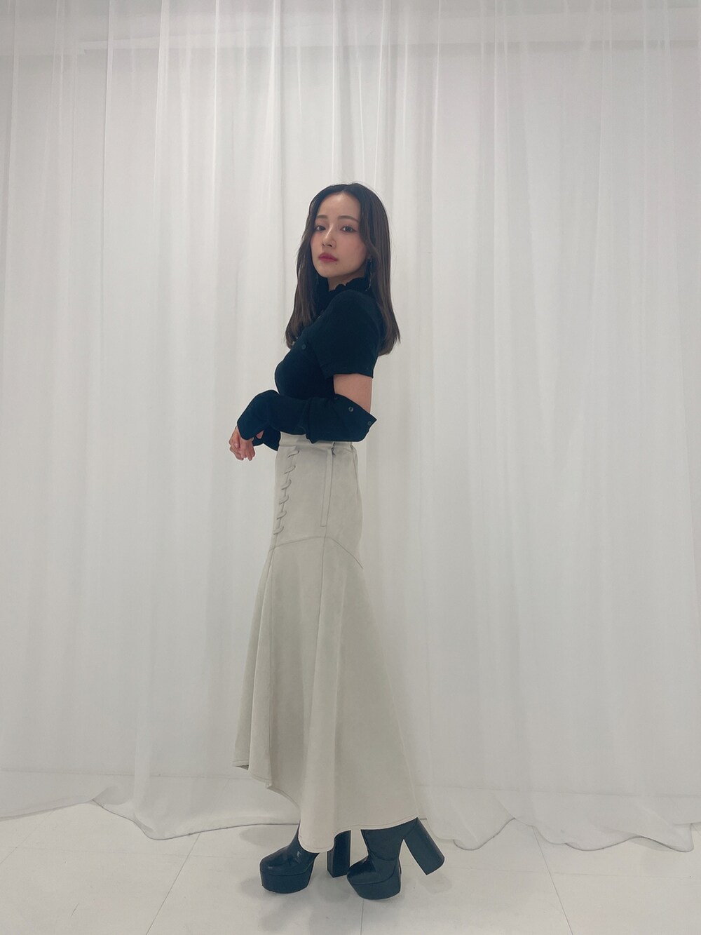 ブラック系のニット/セーター、ホワイト系のスカート、ブラック系のブーツを着用したレディースの春コーディネートの3枚目の写真