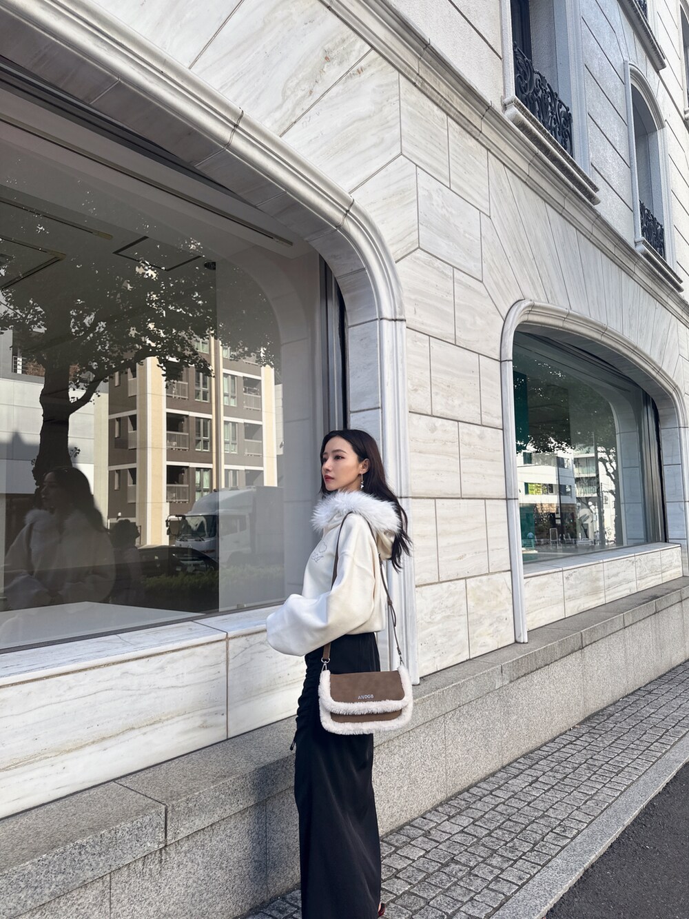 ブラウン系のショルダーバッグ、ホワイト系のパーカー、ブラック系のスカートを着用したレディースの冬コーディネートの5枚目の写真