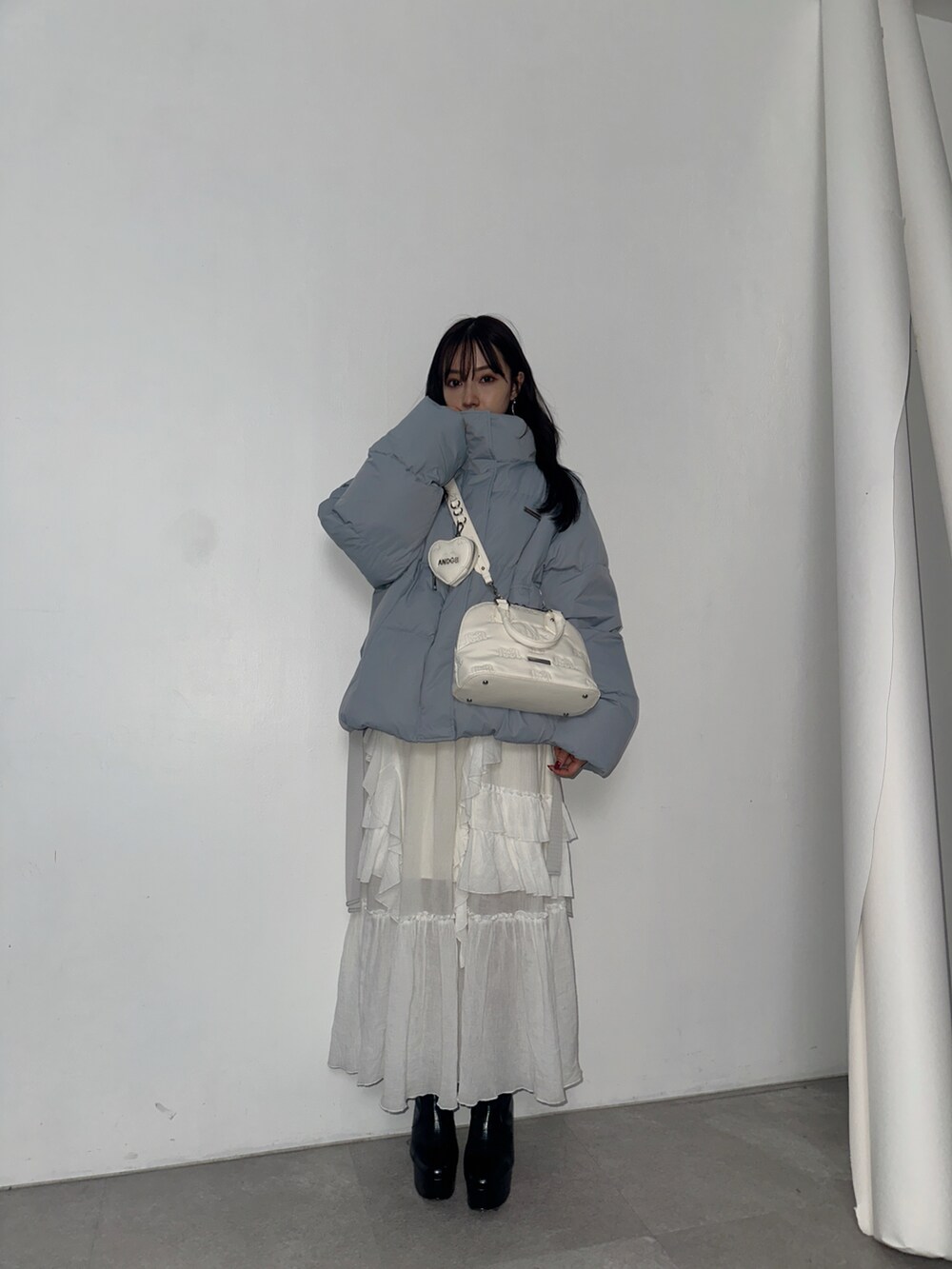 ホワイト系のスカート、グレー系のショルダーバッグ、ブルー系のダウンジャケット/コートを着用したレディースの春コーディネートの2枚目の写真