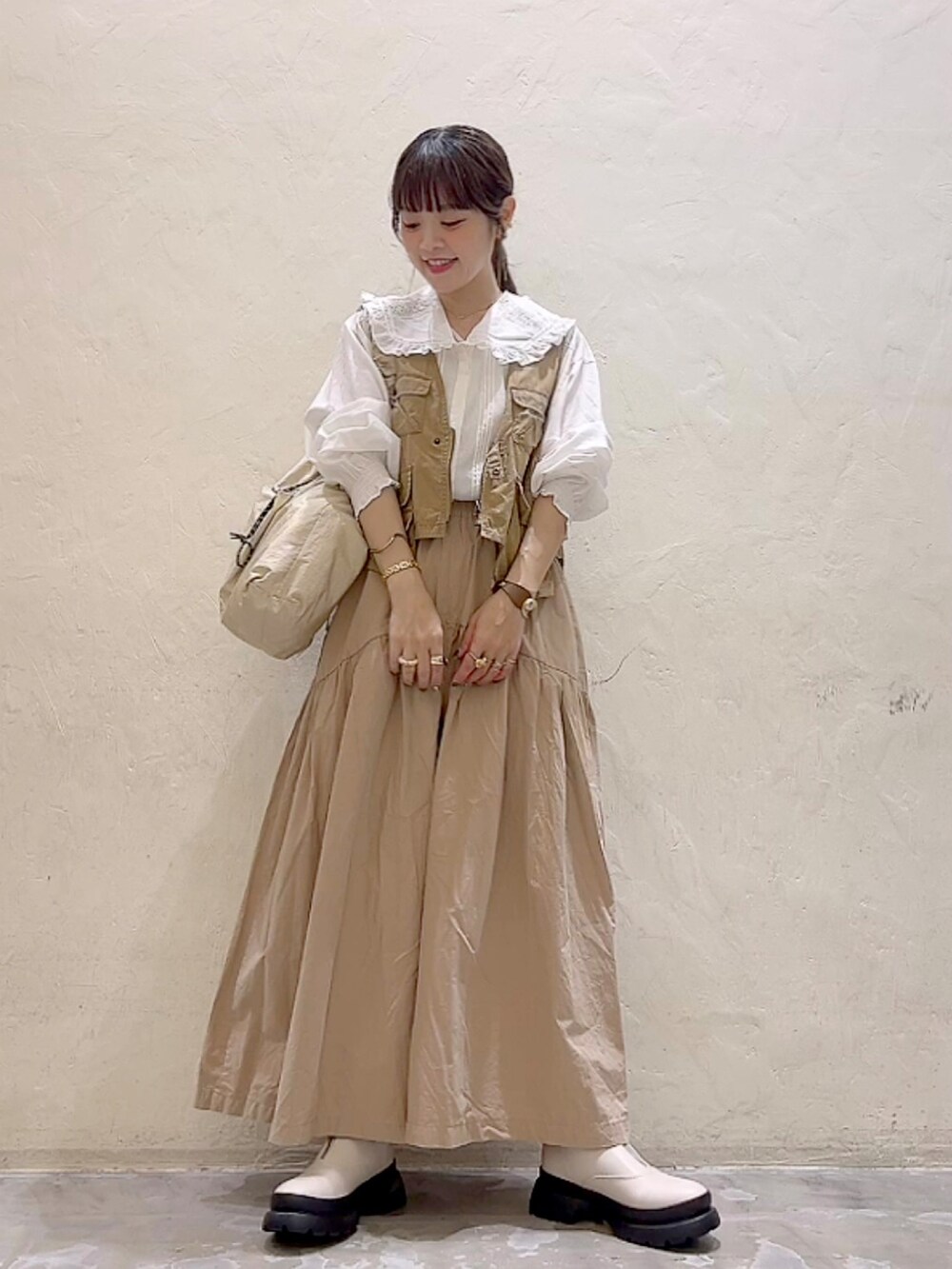 ベージュ系のベスト、ベージュ系のパンツ、ベージュ系のトートバッグを着用したレディースの秋コーディネートの2枚目の写真