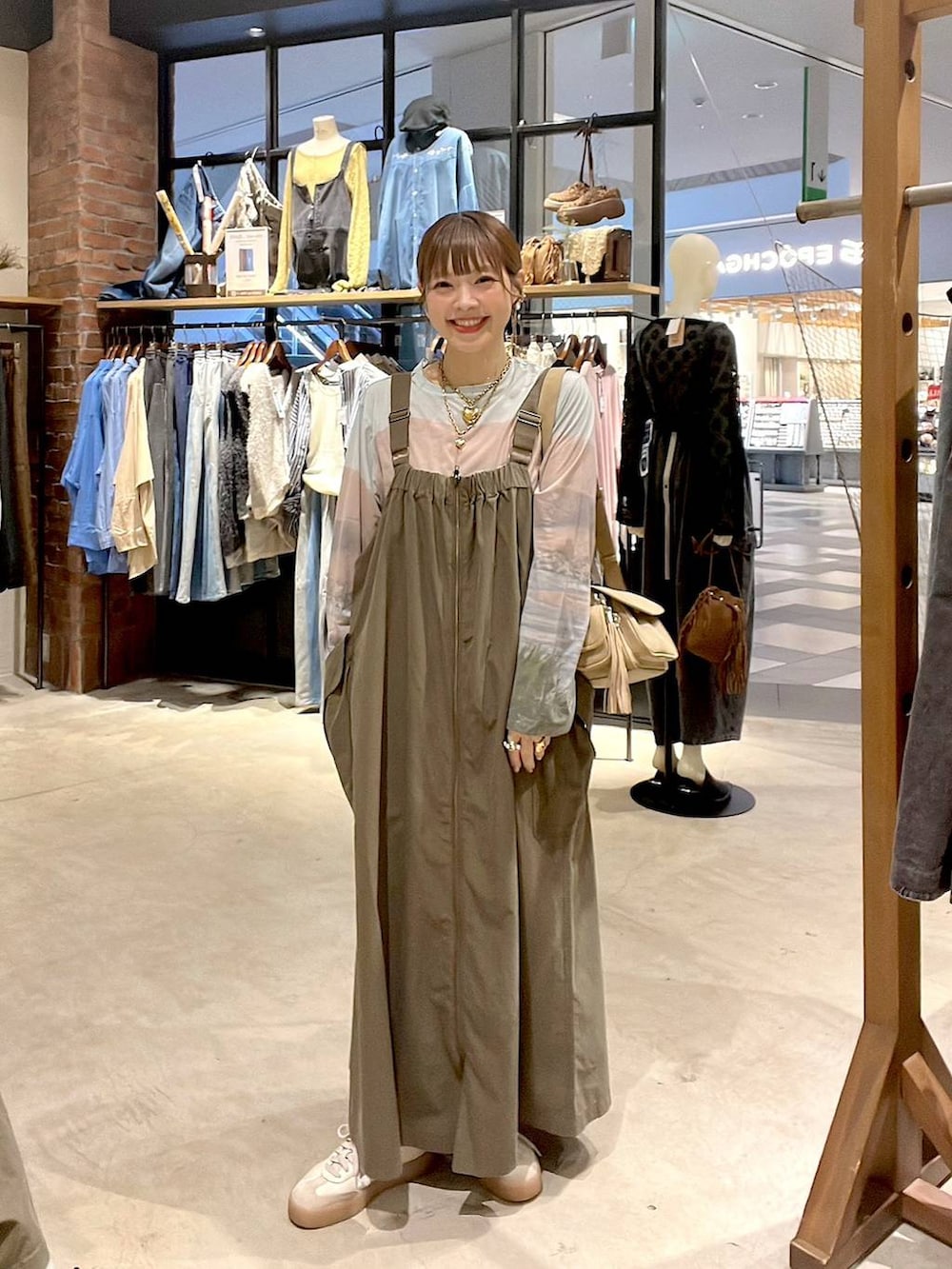 ベージュ系のTシャツ/カットソー、ベージュ系のショルダーバッグ、グリーン系のジャンパースカートを着用したレディースの夏コーディネートの5枚目の写真