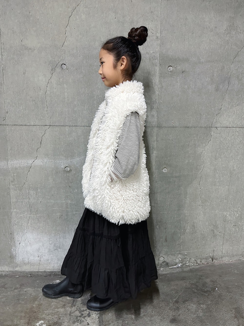 ホワイト系のベスト、ホワイト系のTシャツ/カットソー、ブラック系のスカートを着用したキッズの秋コーディネートの2枚目の写真
