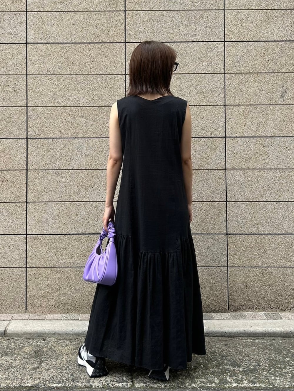 パープル系のハンドバッグ、ブラック系のスニーカー、ブラック系のワンピースを着用したレディースの夏コーディネートの2枚目の写真