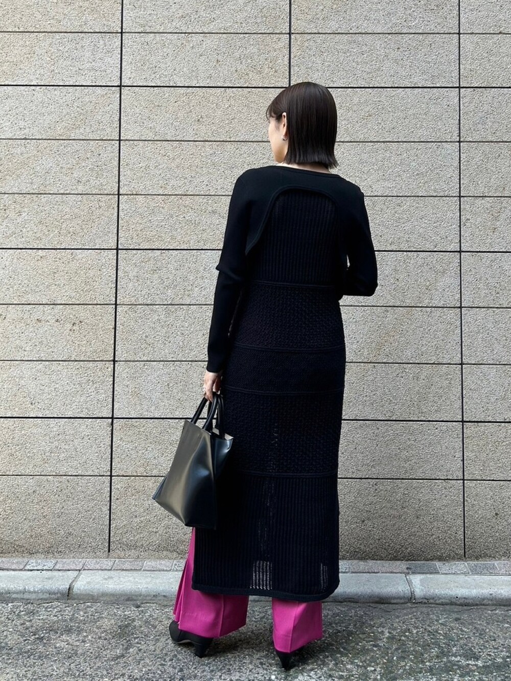ピンク系のパンツ、ブラック系のニット/セーター、ブラック系のワンピースを着用したレディースの春コーディネートの2枚目の写真