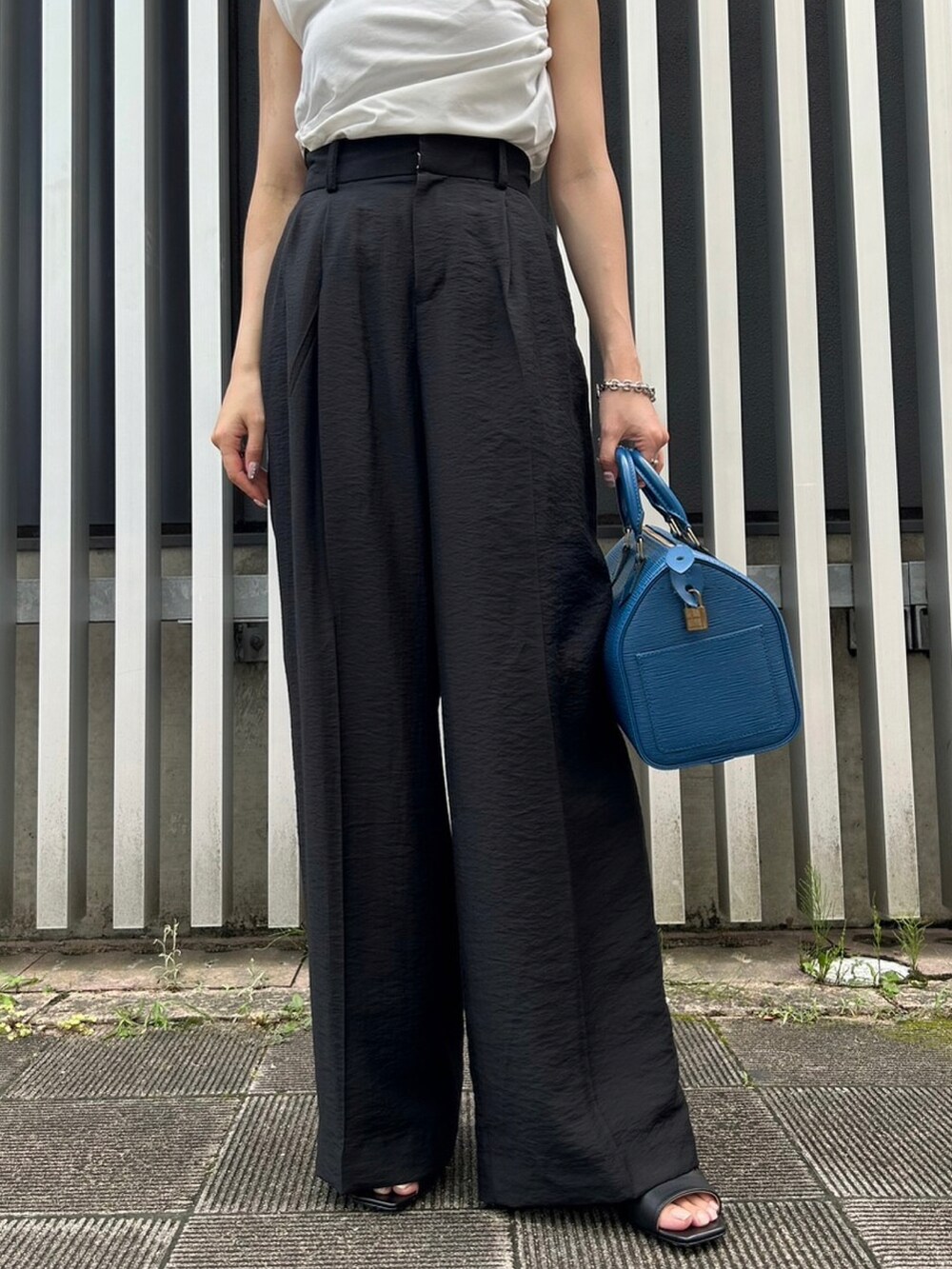 ブラック系のスラックス、ホワイト系のTシャツ/カットソー、ブラック系のサンダルを着用したレディースの夏コーディネートの3枚目の写真