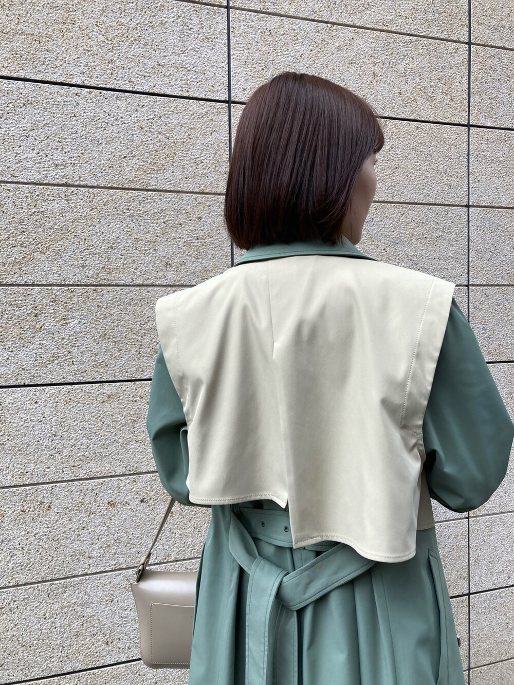 ベージュ系のハンドバッグ、グリーン系のトレンチコート、ブラック系のブーツを着用したレディースの冬コーディネートの2枚目の写真