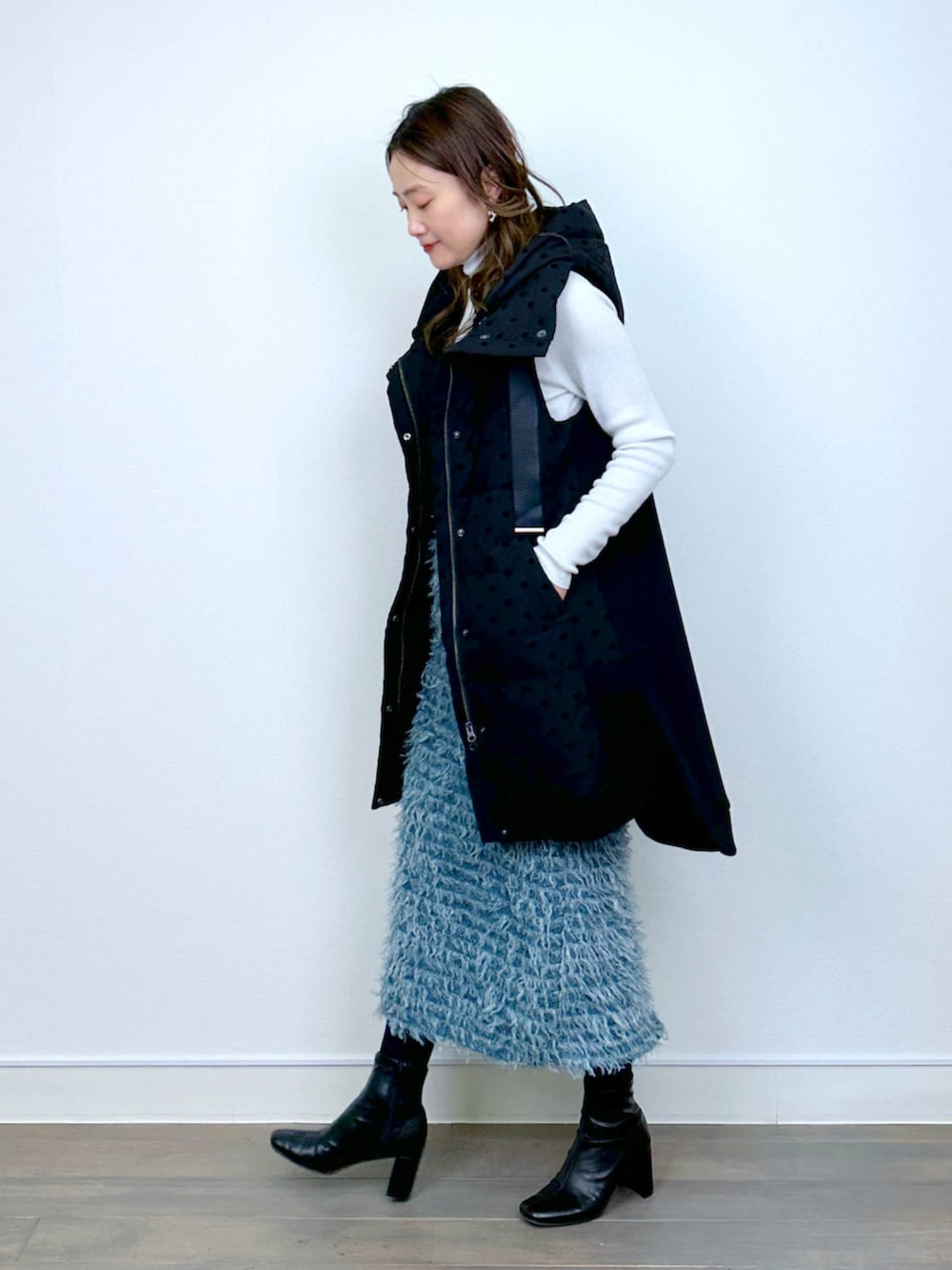 ブラック系のダウンベスト、ホワイト系のニット/セーター、ブルー系のスカートを着用したレディースの冬コーディネートの4枚目の写真