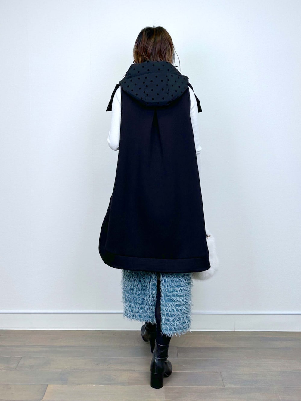 ブラック系のダウンベスト、ホワイト系のニット/セーター、ブルー系のスカートを着用したレディースの冬コーディネートの3枚目の写真