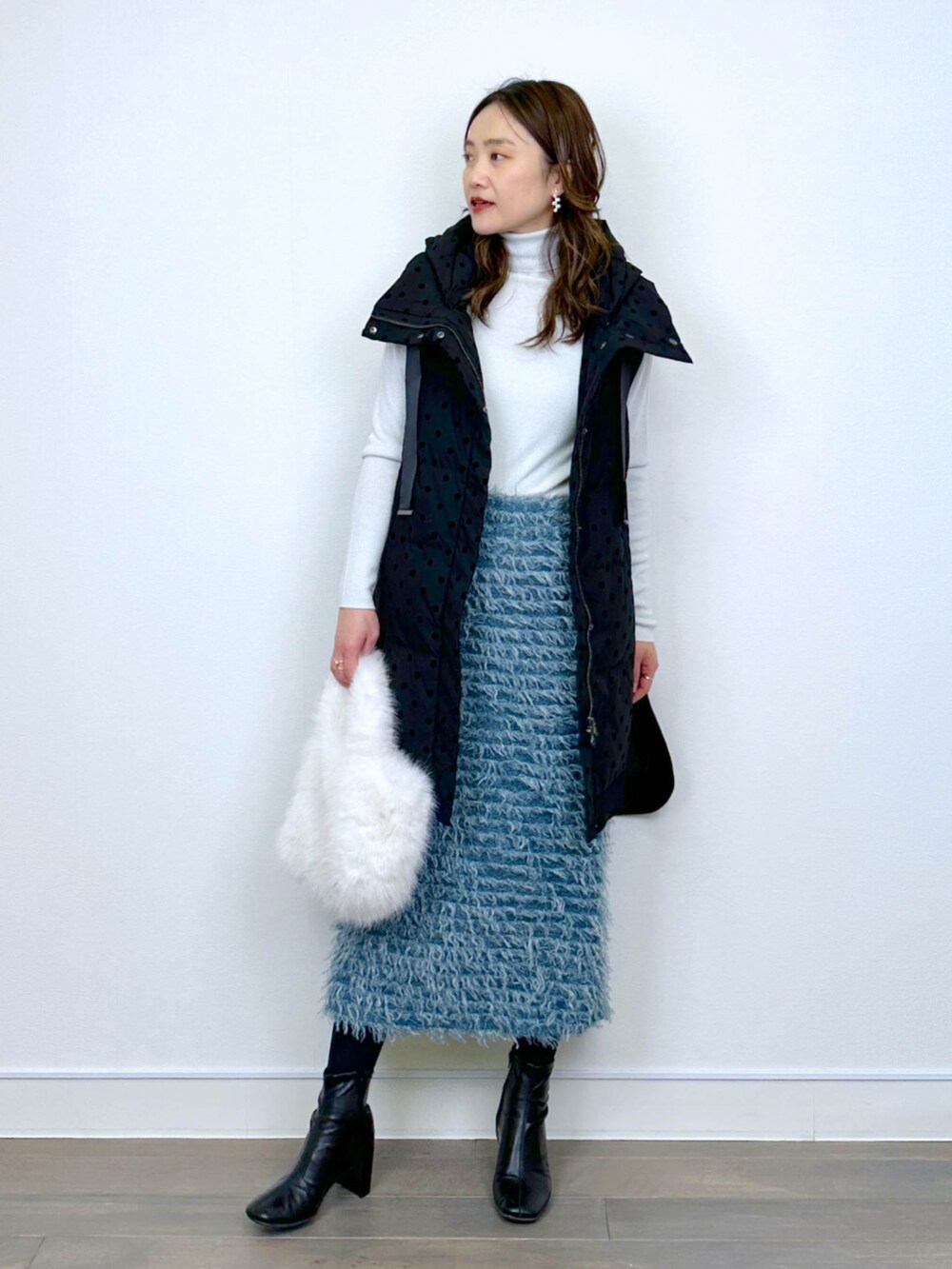 ブラック系のダウンベスト、ホワイト系のニット/セーター、ブルー系のスカートを着用したレディースの冬コーディネートの5枚目の写真