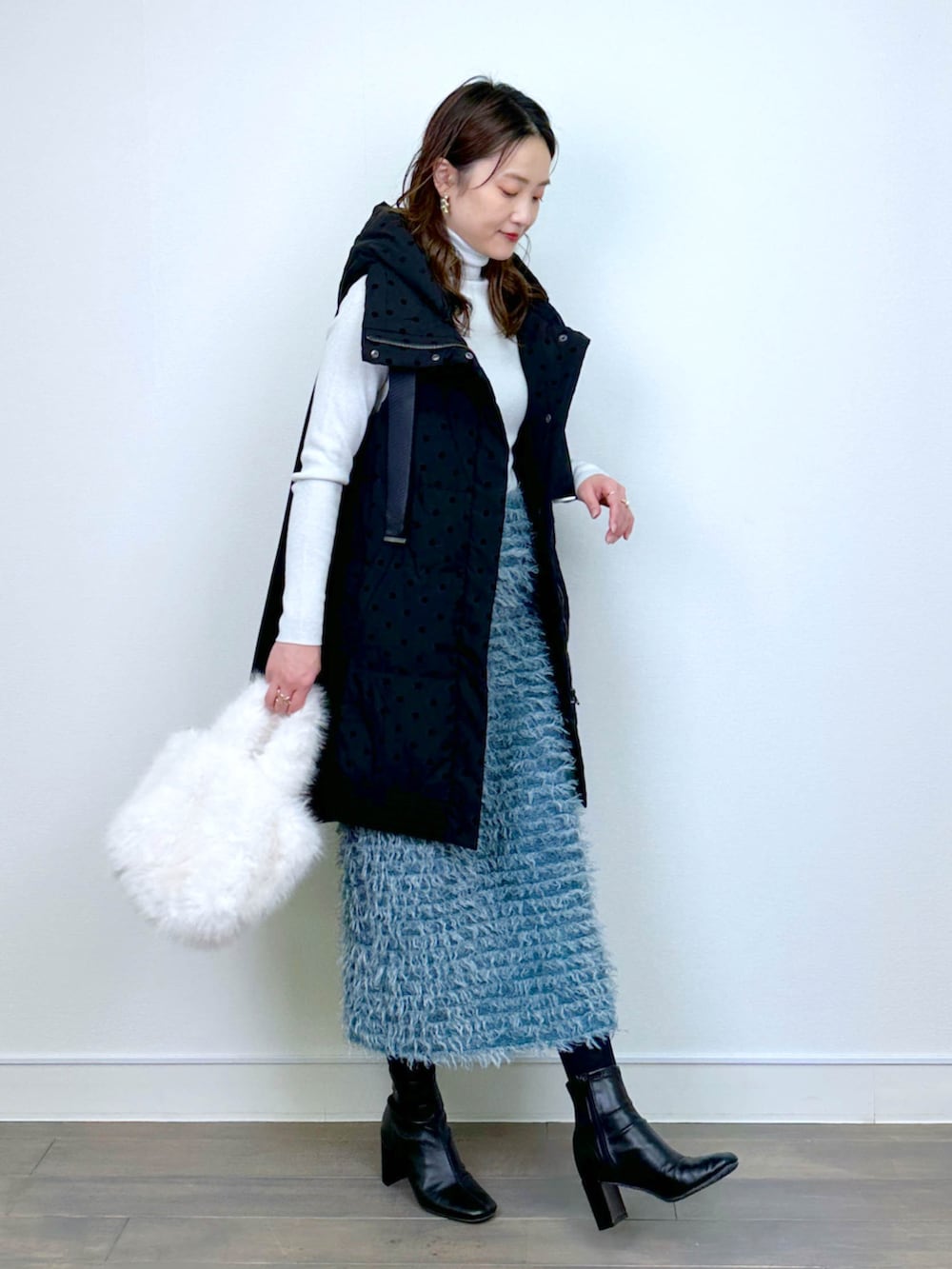 ブラック系のダウンベスト、ホワイト系のニット/セーター、ブルー系のスカートを着用したレディースの冬コーディネートの2枚目の写真