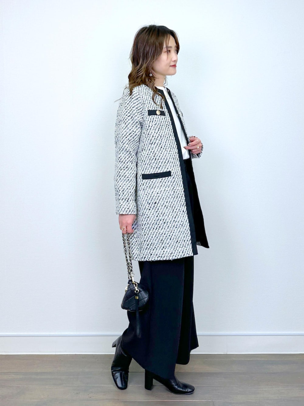 ブラック系のノーカラーコート、ホワイト系のニット/セーター、ブラック系のその他パンツを着用したレディースの冬コーディネートの2枚目の写真