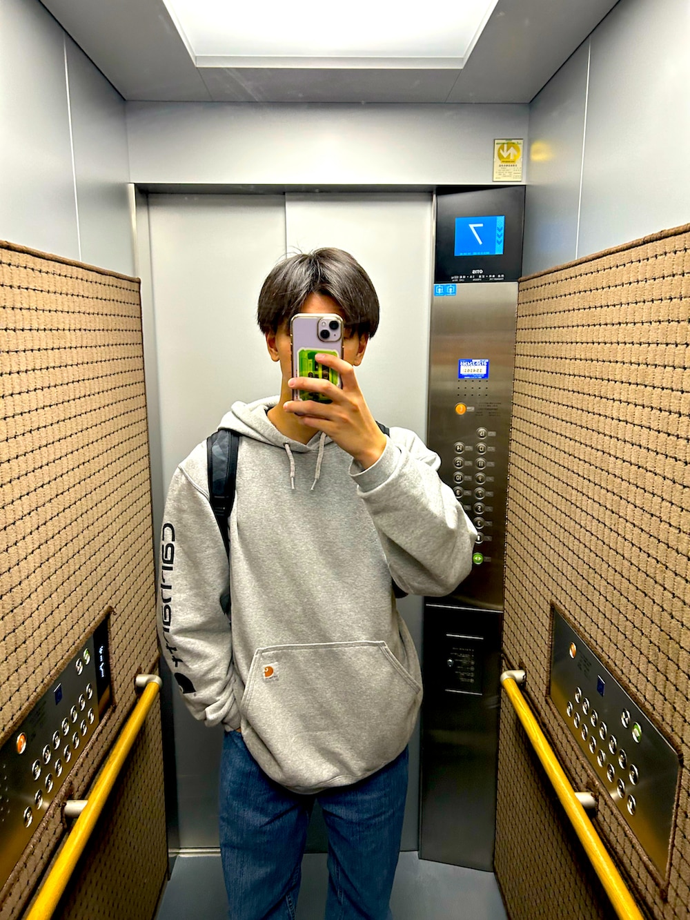 グレー系のパーカー、ブラック系のスニーカー、ブルー系のデニムパンツを着用したメンズの秋コーディネートの2枚目の写真